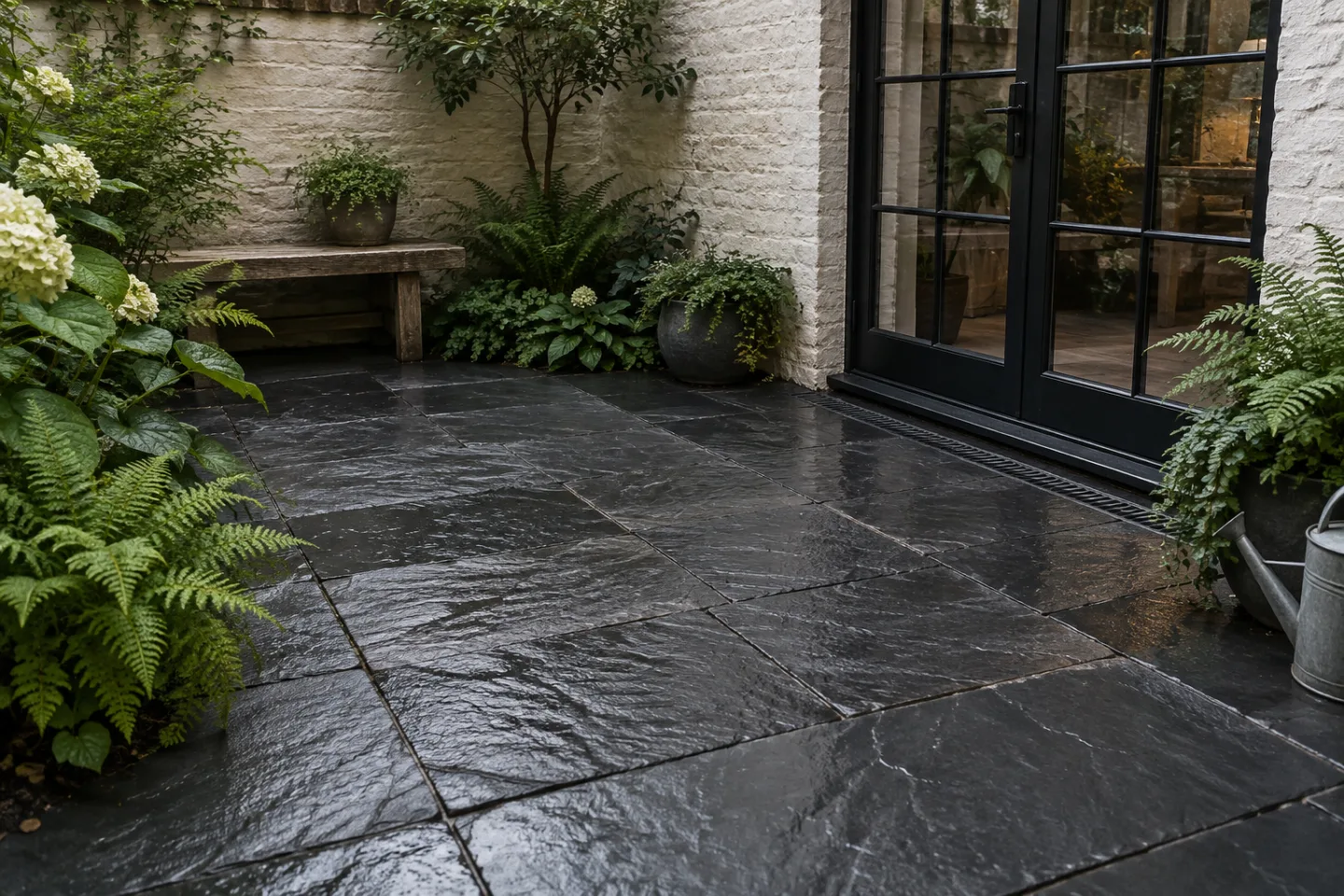 Dark riven slate patio in a sheltered planted courtyard after rain
